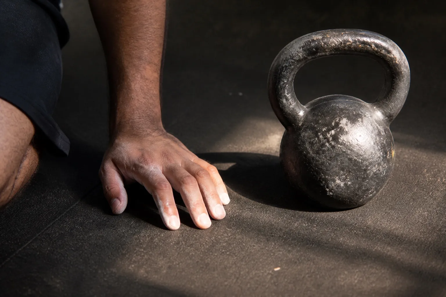 A chalked hand rests beside a kettlebell between sets during a high-volume session.