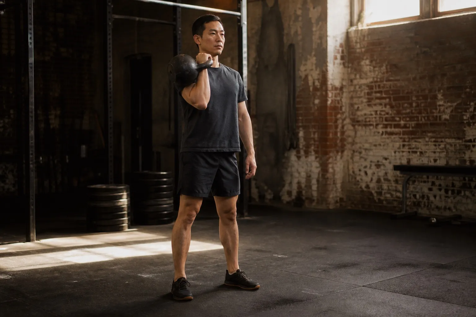 A man holds a kettlebell in the rack position before an overhead press.