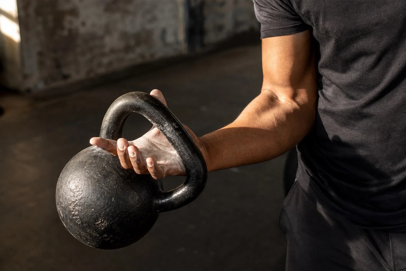 A close view shows a hand passing through a kettlebell handle as the bell turns gently around the wrist toward the rack.